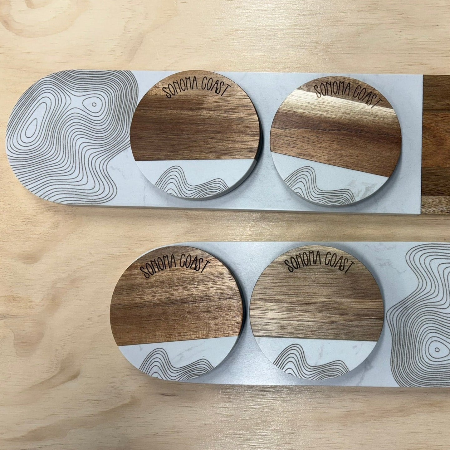 Two wooden coasters with a white center and gray pattern on a wooden surface.